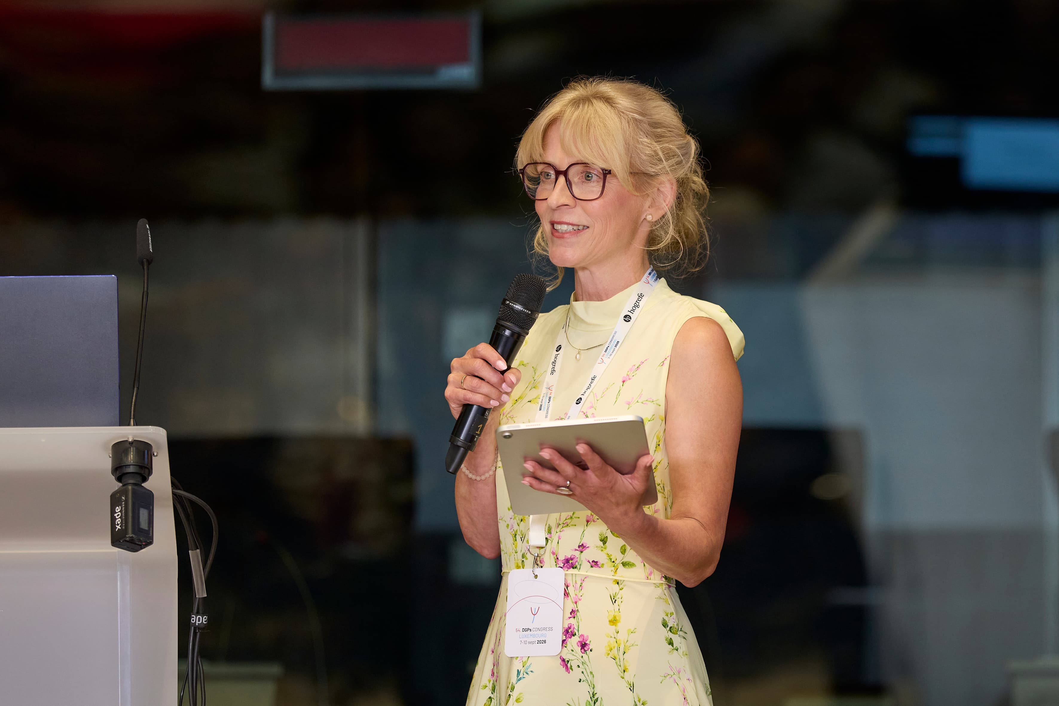 A speaker addresses the audience with a handheld microphone during the opening ceremony of the 54th DGPs Congress in Luxembourg.