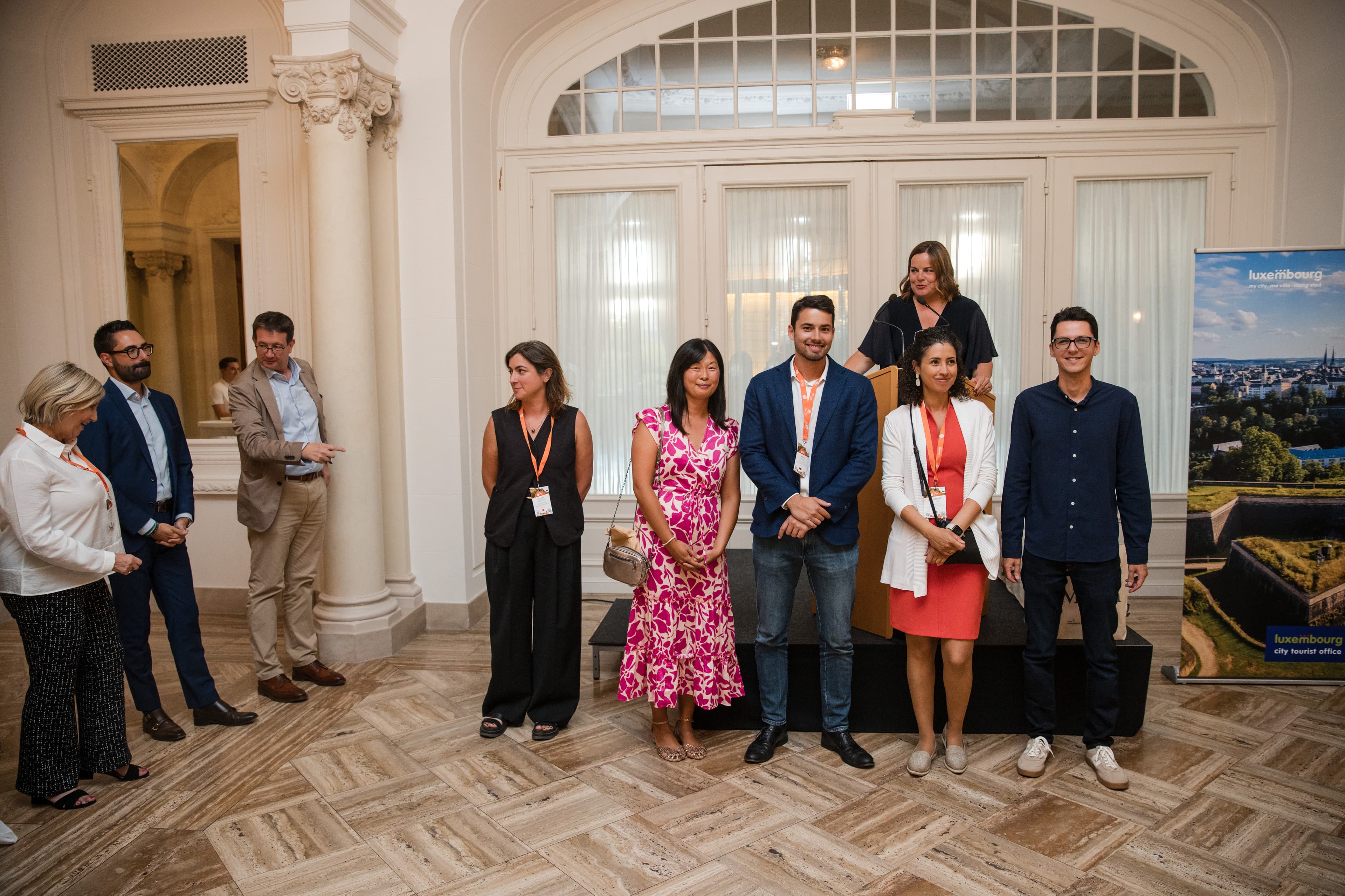 A group stands beside a lectern in an elegant classical room at a Luxembourg City Tourist Office reception