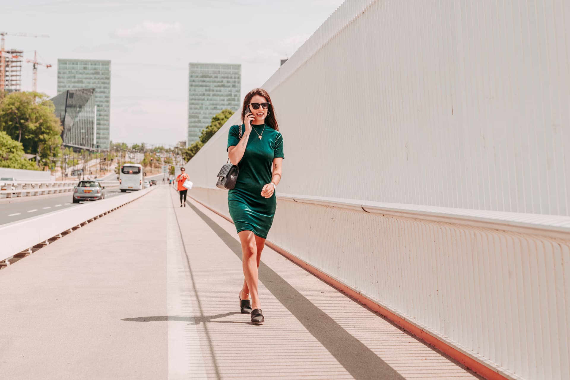 A woman on her phone walks along a bridge with the Kirchberg towers behind in Luxembourg