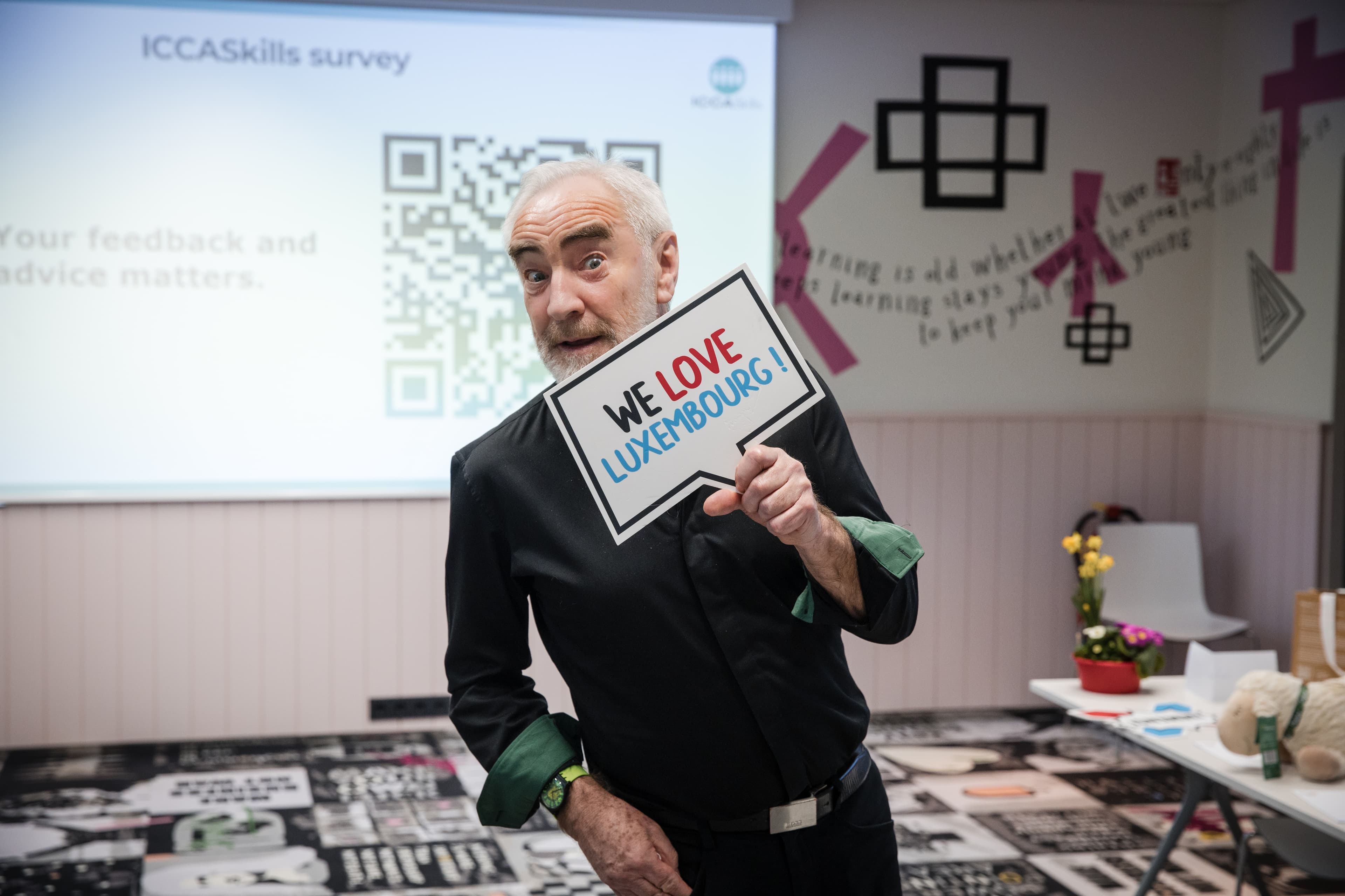A man holding a sign that says "WE LOVE LUXEMBOURG!" in front of a presentation screen.