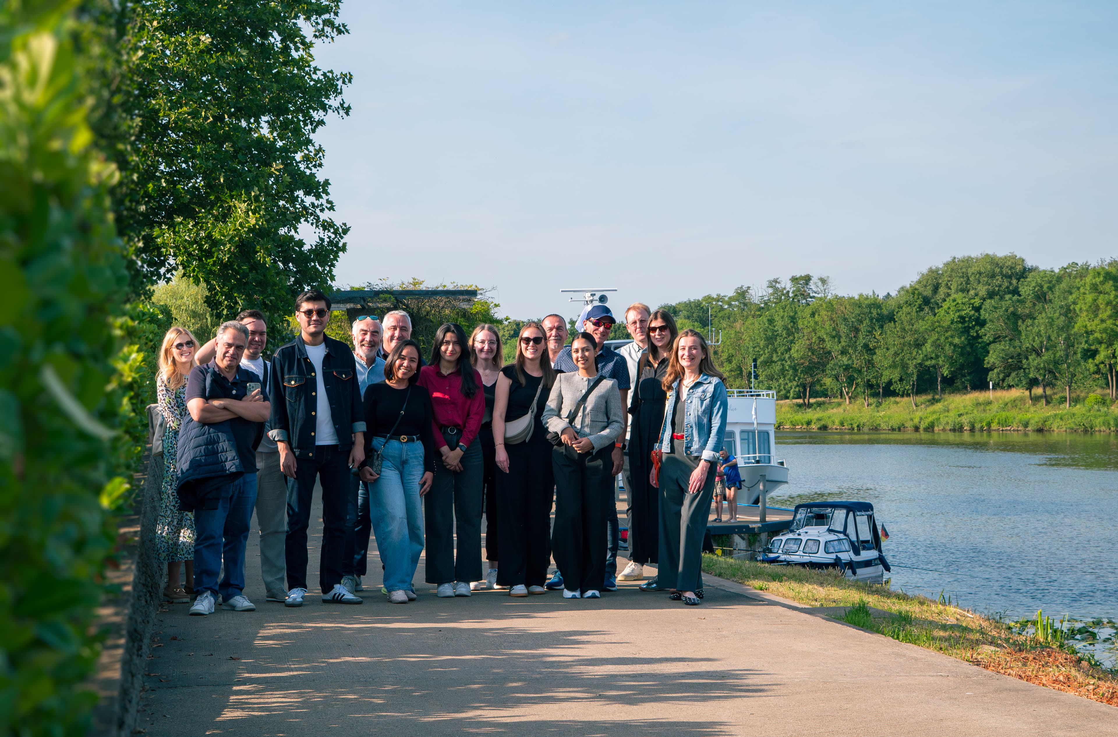 A group posing together on a riverside path with boats moored on a sunny day